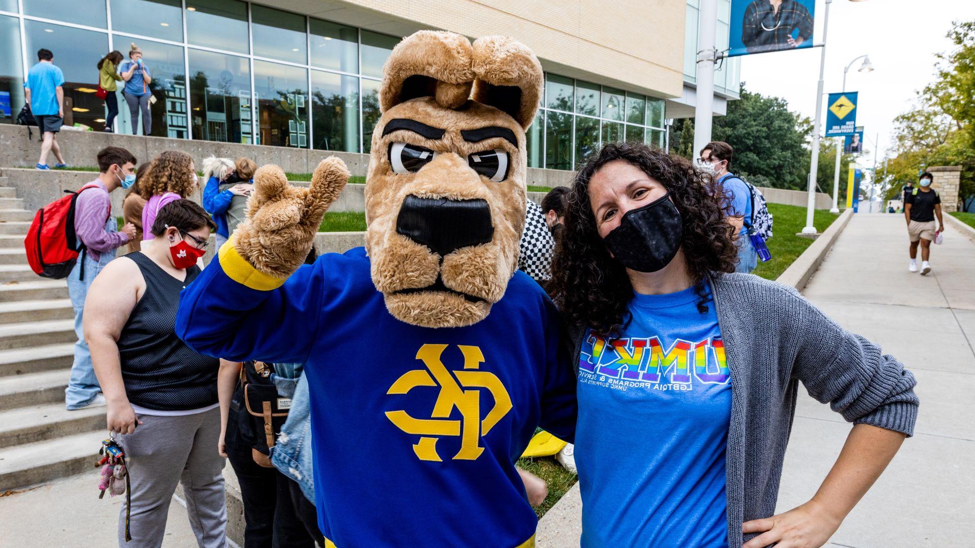 woman wearing a mask stands next to Kacey the umkc kangaroo mascot